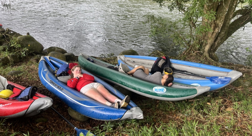 two people rest in beached watercraft on the shore of a river